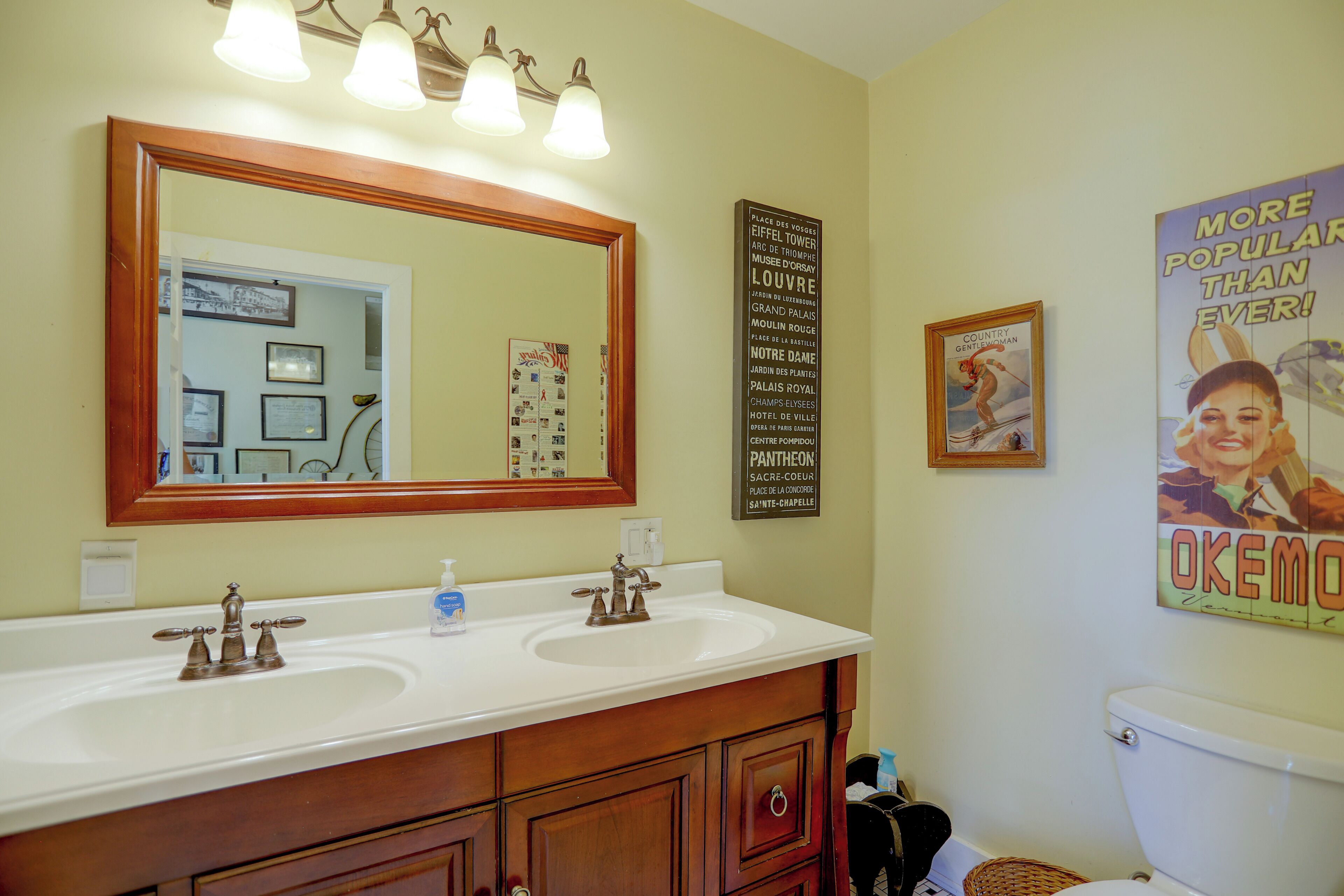 A bathroom with a double sink vanity, a large mirror, and a poster on the wall.