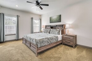 Un dormitorio con cama, mesitas de noche, ventilador de techo y ventana con cortinas.