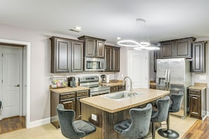 A modern kitchen with dark wood cabinets, stainless steel appliances, a central island with bar stools, and a pendant light. - Extended Stay Gem Near Redstone Arsenal & Airport (Madison)