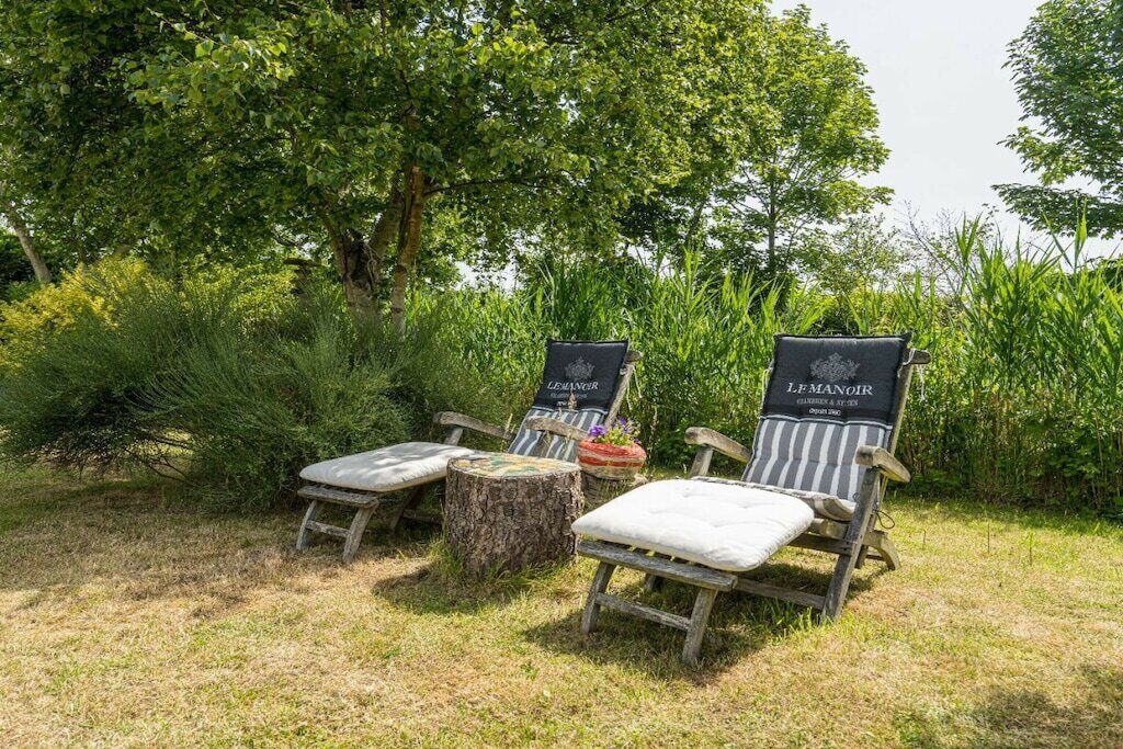 Deux fauteuils de jardin avec coussins, un tronc d’arbre servant de table basse et une petite table avec un pot de fleurs.