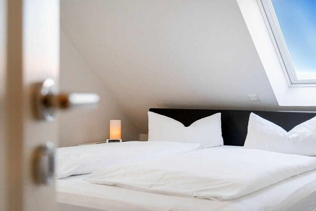 Ein Schlafzimmer mit Dachfenster, einem Bett mit weißer Bettwäsche und einem Nachttisch mit Lampe.