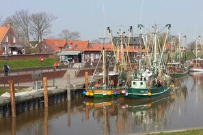 Ein Hafen mit vertäuten Booten, einem Fußweg und Gebäuden im Hintergrund.