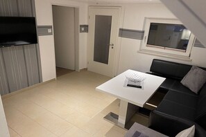 A modern interior with a white table, black sofa, and a TV mounted on the wall. - Holiday apartment 3, House Johanni (Norderney)