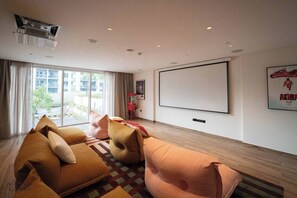 A modern living room with a large window, a projector screen, and a sofa set. - New Cozy 1BR | Dubai Hills (Dubai)