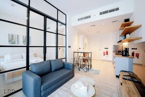 Une chambre d’hôtel moderne dotée d’un canapé, d’un coin repas avec une table et des chaises, d’une kitchenette et d’une grande fenêtre offrant une vue dégagée.