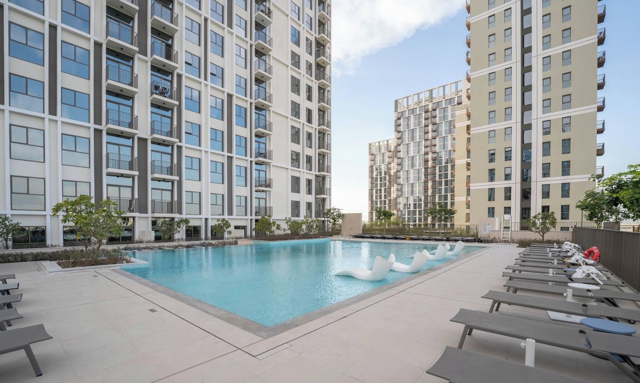 A modern apartment building with a swimming pool and lounge chairs.