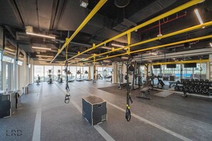 Une salle de sport spacieuse équipée de divers appareils d’exercice, notamment des tapis de course, des appareils de musculation et des sangles de suspension.