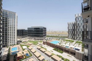A modern residential complex with multiple high-rise buildings, a central courtyard with a swimming pool, and a view of the surrounding area. - New Cozy 1BR | Dubai Hills (Dubai)