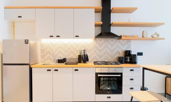 Une cuisine compacte avec des meubles blancs, un four encastré, une cuisinière à gaz et une machine à café.