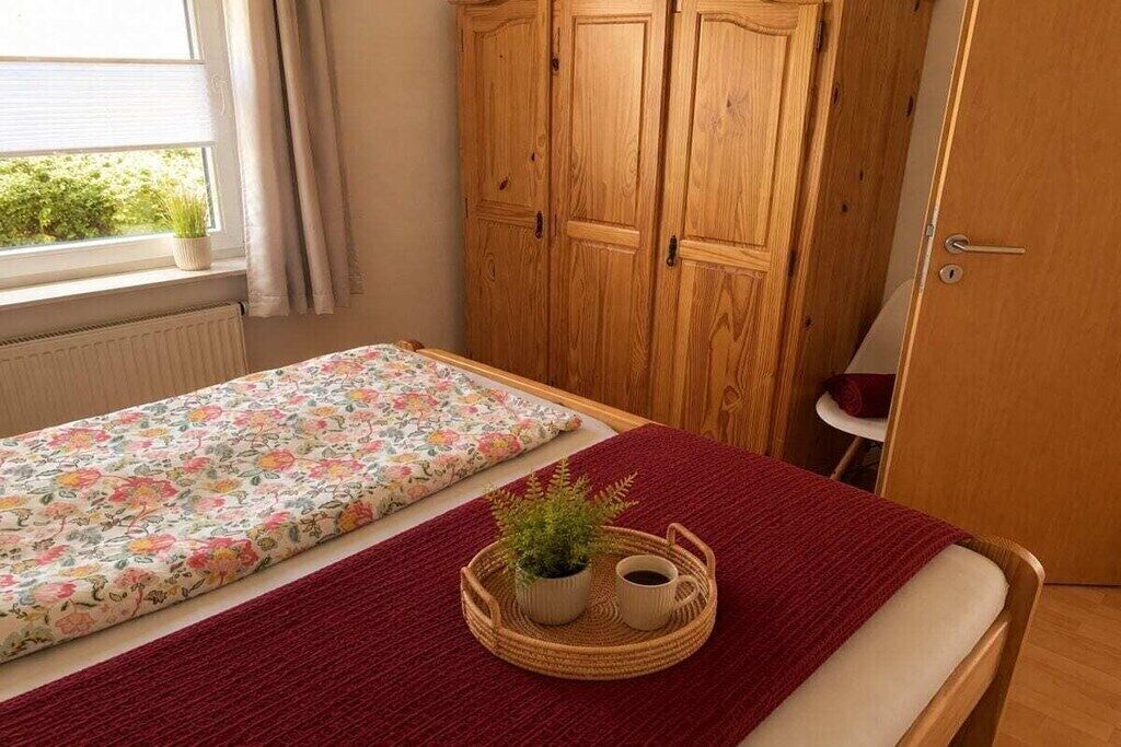 Ein Schlafzimmer mit einem Bett, einem Holzschrank, einem Fenster mit Vorhängen und einer kleinen Pflanze auf einer Ablage.