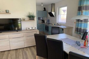 Una cuina moderna amb zona de menjador, televisió de pantalla plana i finestra amb cortines.