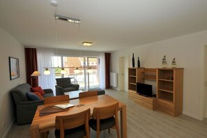 A modern living room with a dining area, a TV stand, and a view of the outdoors. - "Seestern", in the House of Recreation (Juist)