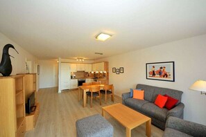 A modern living room with a grey sofa, wooden coffee table, and a dining area with a wooden table and chairs. - "Seestern", in the House of Recreation (Juist)