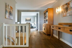 A hallway with a wooden floor, a white railing, a wooden cabinet, and a desk with drawers. - Holiday apartment with 3 bedrooms (Hörnum \/ Sylt)