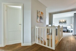 Ein Flur mit einer weißen Tür, einem weißen Geländer und einer Treppe, die zu einem Raum mit einem grauen Sofa und einem Gemälde an der Wand führt.