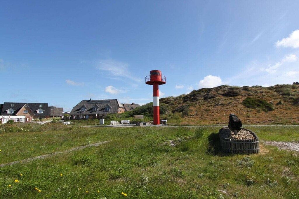 A lighthouse with a red and white structure, surrounded by a grassy field and a hill in the background.