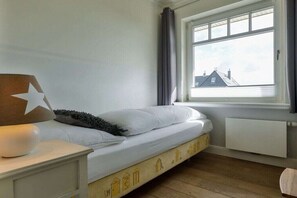 Ein Schlafzimmer mit einem Einzelbett, einem Nachttisch mit Lampe, einem Fenster mit Vorhängen und einer Heizung.