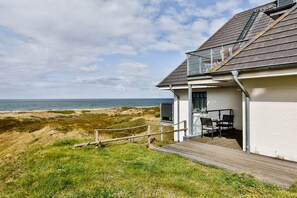 A coastal house with a deck overlooking the sea, a small outdoor seating area, and a clear view of the beach. - Holiday apartment with 3 bedrooms (Hörnum \/ Sylt)
