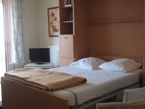 Una camera d'hotel con un letto, una televisione su un tavolino, un armadio in legno e un quadro appeso al muro.
