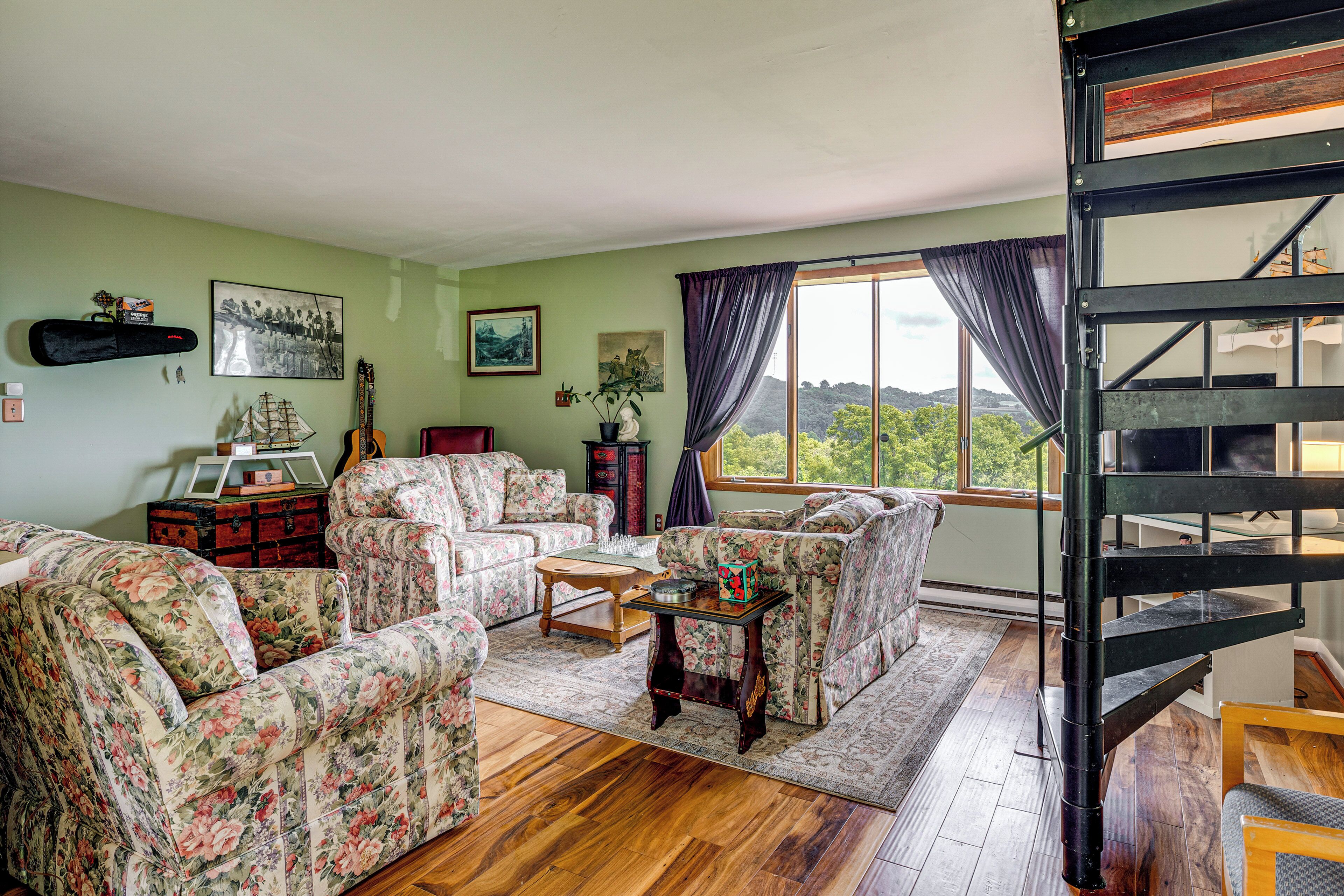 Un salon meublé de meubles à motifs floraux, avec une table basse en bois et une vue sur un paysage verdoyant par la fenêtre.