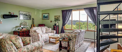 A living room with floral-patterned furniture, a wooden coffee table, and a view of a green landscape through a window.