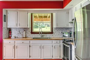 A kitchen with white cabinets, a stainless steel refrigerator, a microwave, and a window with a view of greenery. - Bangor Countryside Retreat w/ Gorgeous Views (Bangor)