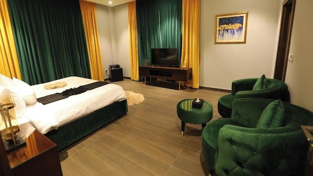 Une chambre d’hôtel avec un lit, une télévision, un bureau et un fauteuil vert.