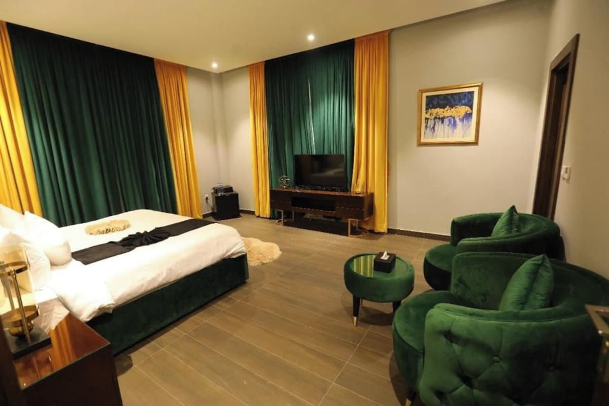 Une chambre d’hôtel avec un lit, une télévision, un bureau et un fauteuil vert.