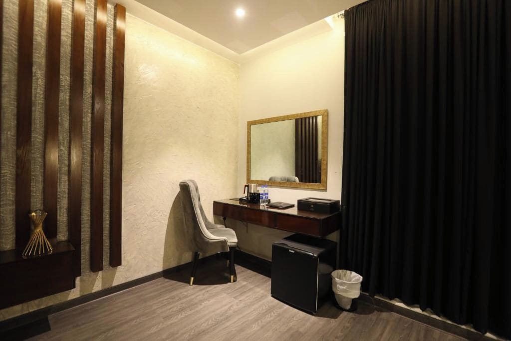 Habitación de hotel con escritorio, silla, espejo y un refrigerador pequeño.