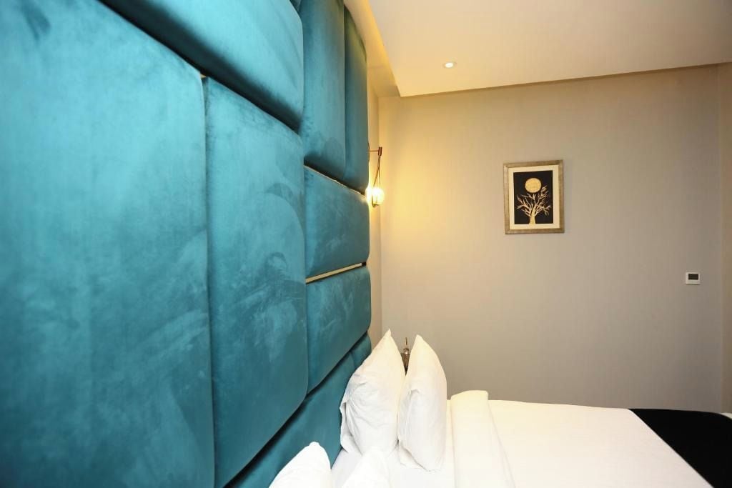 Habitación de hotel con una cama grande, cabecera color turquesa, luz de pared e imagen enmarcada.