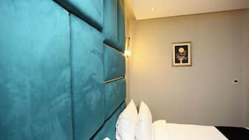 Habitación de hotel con una cama grande, cabecera color turquesa, luz de pared e imagen enmarcada.