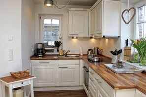 A compact kitchen with white cabinets, a wooden countertop, a coffee maker, and a heart-shaped decoration on the wall. - Holiday home in Hörnum with 3 bedrooms (Hörnum \/ Sylt)