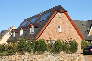 A residential building with a sloped roof, multiple windows, and a stone wall in front. - Holiday home in Hörnum with 3 bedrooms (Hörnum \/ Sylt)