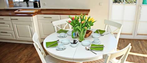 A dining area with a round table set for four, surrounded by white chairs with striped cushions.