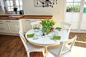 A dining area with a round table set for four, surrounded by white chairs with striped cushions. - Holiday home in Hörnum with 3 bedrooms (Hörnum \/ Sylt)