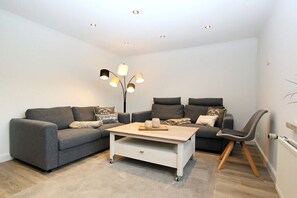 A modern living room with two grey sofas, a white coffee table, and a unique floor lamp. - Holiday apartment with 2 bedrooms (Hörnum \/ Sylt)
