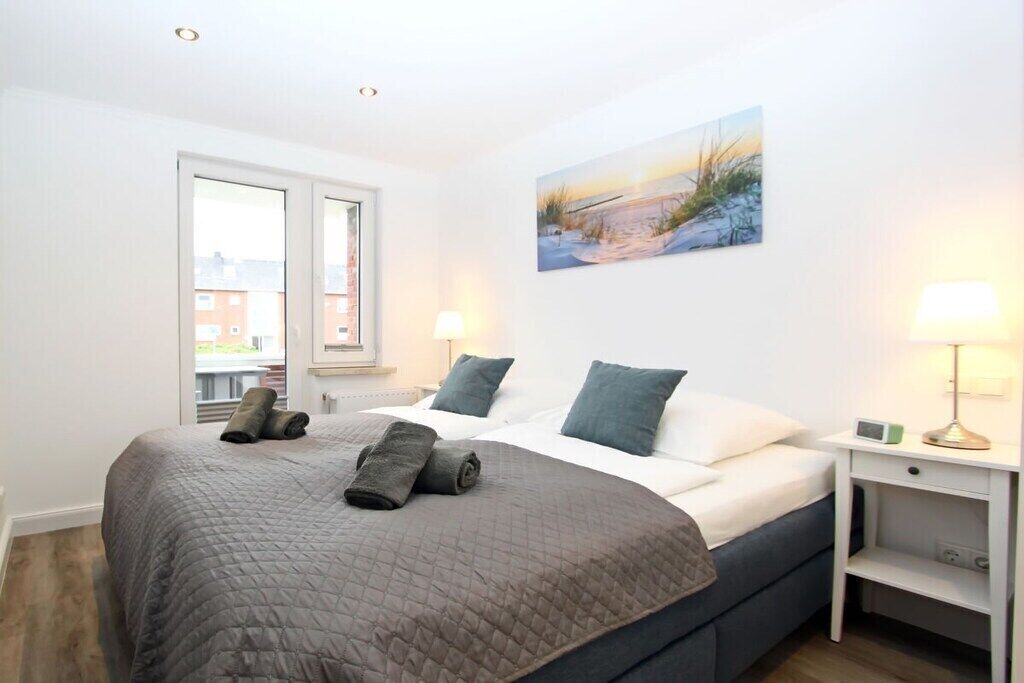 A bedroom with a bed, pillows, a bedside table, a lamp, and a painting on the wall.