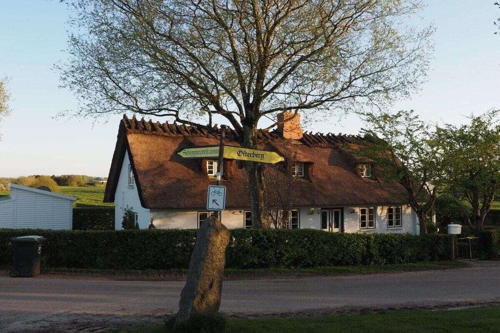 A traditional thatched-roof house with a signpost indicating directions to nearby locations.