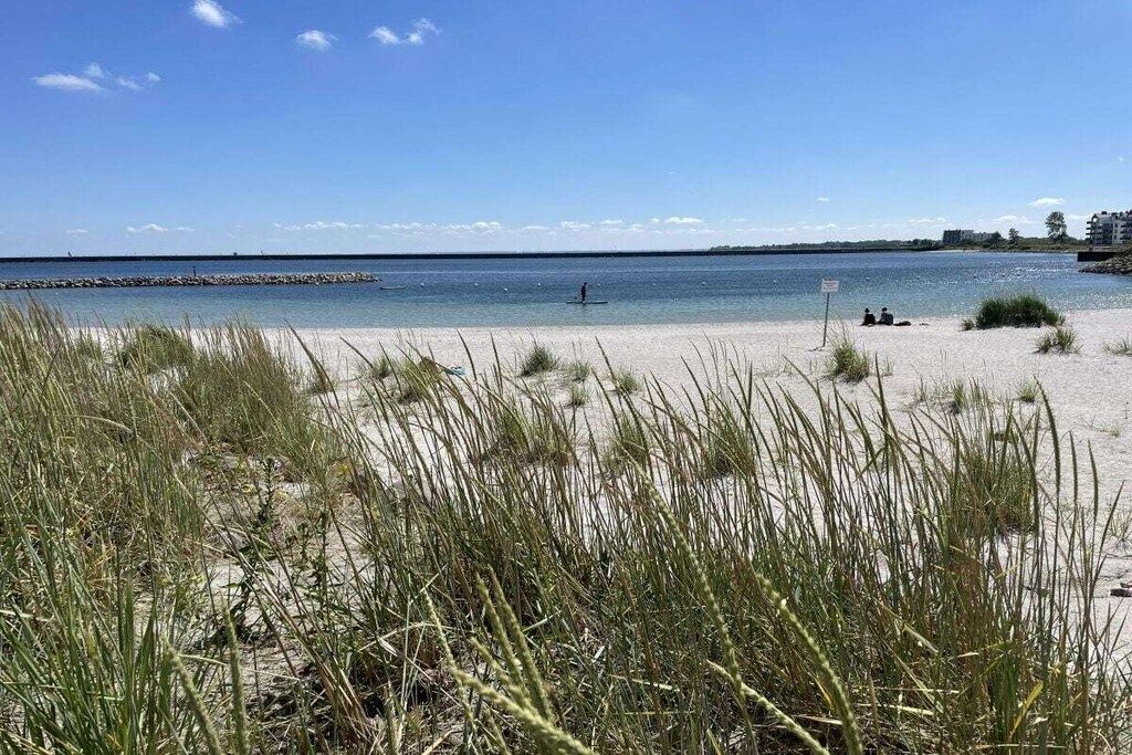A beach with sand, grass, and a calm body of water.