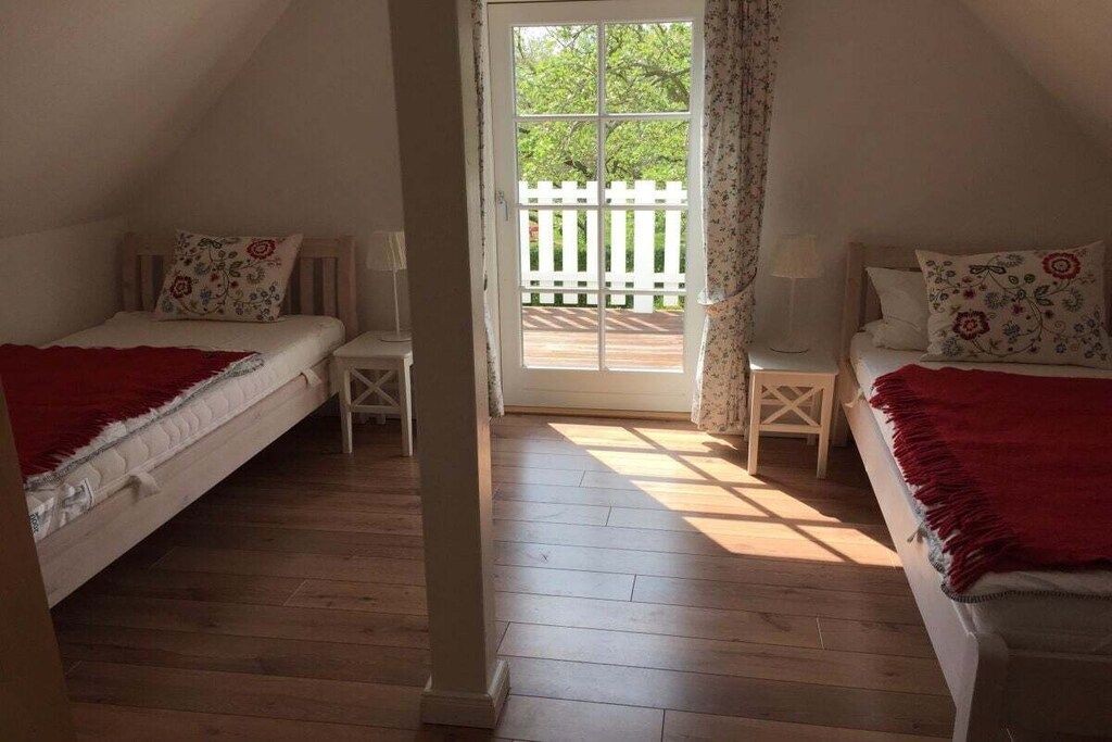 A bedroom with two beds, a wooden floor, a white door leading to an outdoor area, and a small table between the beds.