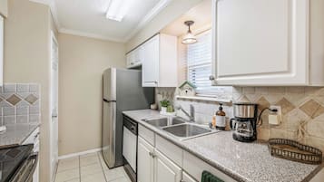 A kitchen with white cabinets, a stainless steel refrigerator, a double sink, and a coffee maker.