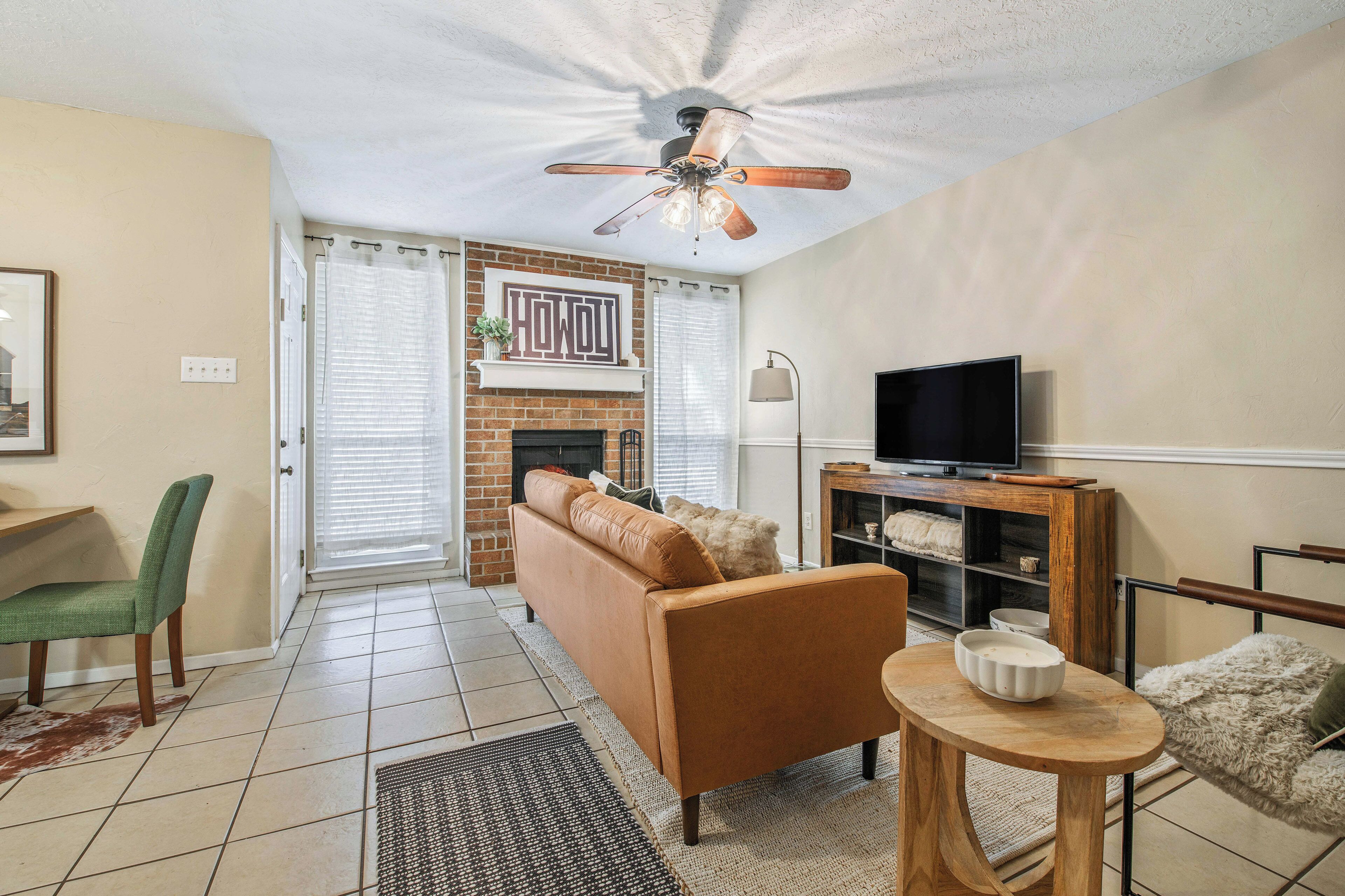 A living room with a fireplace, a sofa, a television on a wooden stand, and a ceiling fan.