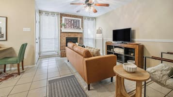 A living room with a fireplace, a sofa, a television on a wooden stand, and a ceiling fan.