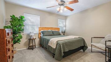 A bedroom with a bed, a dresser, a plant, and a ceiling fan.