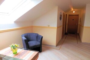 A room with a skylight, a dark armchair, a small table with a vase, and a wooden floor. - Holiday complex Wildt No. 9 (Fehmarn \/ Petersdorf)
