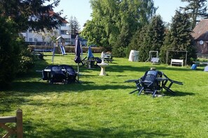 An outdoor area with a grassy lawn, a children's play structure, and several chairs and tables. - Holiday complex Wildt No. 9 (Fehmarn \/ Petersdorf)
