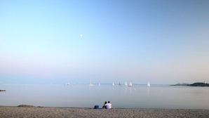A beach with a calm sea, a few sailboats, and two people sitting on the sand. - Pilot station type G (Neustadt\/Holstein - OT Pelzerhaken)