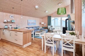 Ein gemütliches Cabin-Interieur mit Holzbalkendecke, einer Essecke mit weißen Stühlen, einer Couch und einer Küchenzeile mit Kücheninsel.