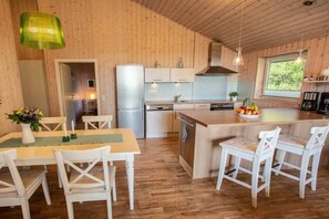 Eine moderne Küche mit Holzwänden, einem Essbereich mit weißen Stühlen und einer großen Kochinsel mit Sitzgelegenheiten.