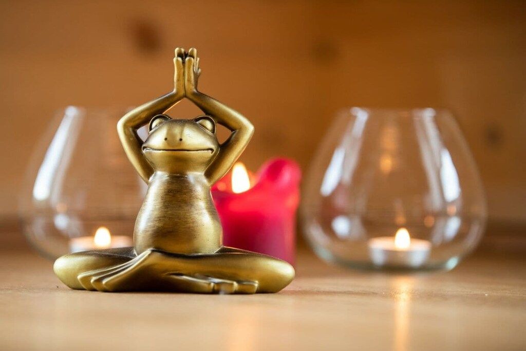 Tapete de yoga em formato de sapo, com uma vela e um castiçal de vidro ao fundo.